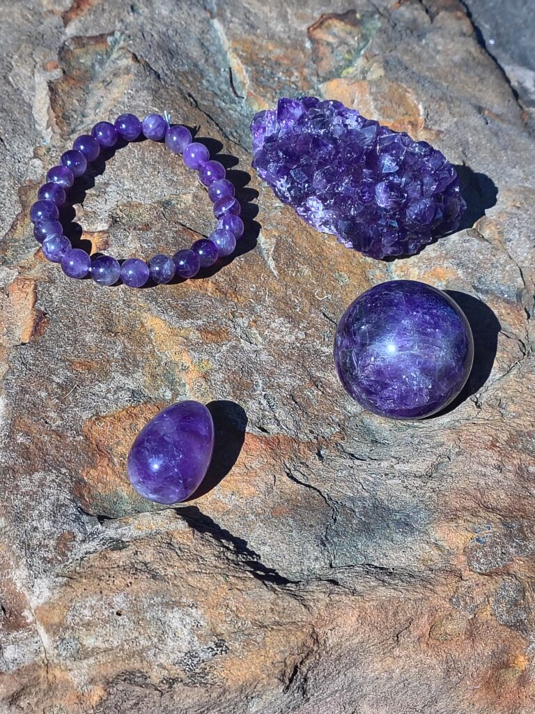 Amethyst crystal bundle with multiple natural purple amethyst pieces arranged together on a rock outdoors.