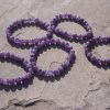 Amethyst bracelet with natural purple beads resting on a rock outdoors.