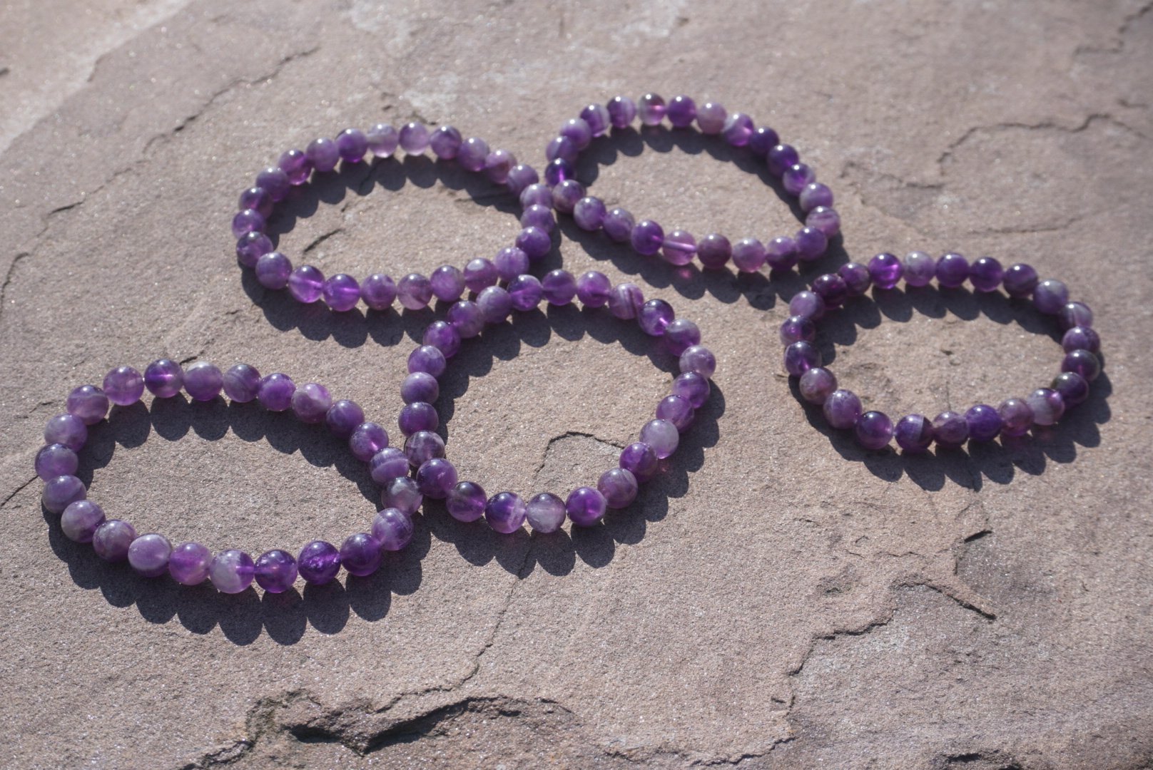 Amethyst bracelet with natural purple beads resting on a rock outdoors.