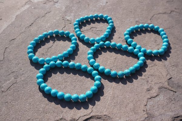 Turquoise bracelet with blue-green beads resting on a natural rock outdoors.