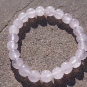Rose Quartz stretch bracelet with soft pink beads and natural variations resting on a rock outdoors