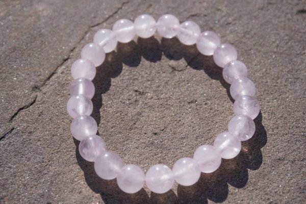 Rose Quartz stretch bracelet with soft pink beads and natural variations resting on a rock outdoors