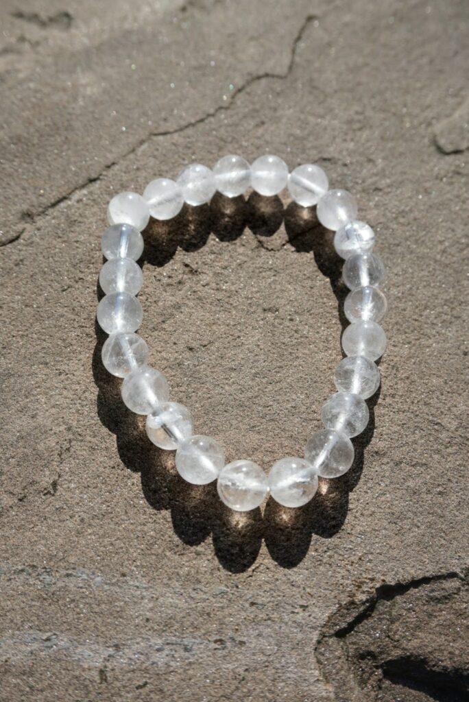 Clear Quartz stretch bracelet with transparent beads and natural inclusions resting on a rock outdoors.