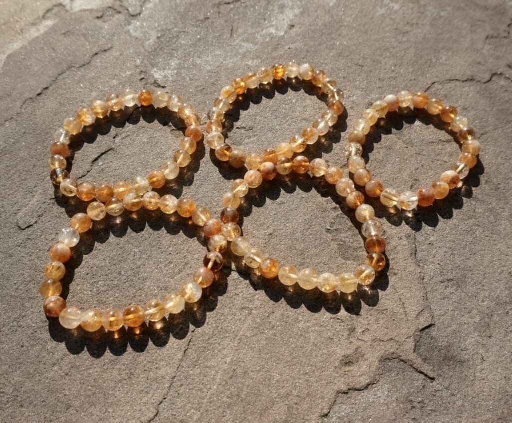 "A close-up of 5 stretch bracelet made from round, polished golden-yellow citrine crystal beads resting on a Rock